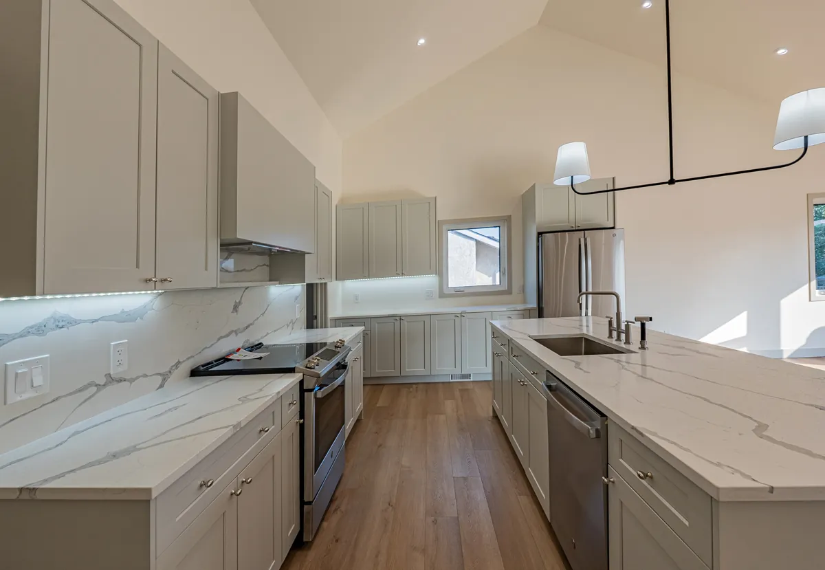 A completed PHS Renovations kitchen in Winnipeg — vaulted ceiling, marble-veined quartz counters and a long centre island